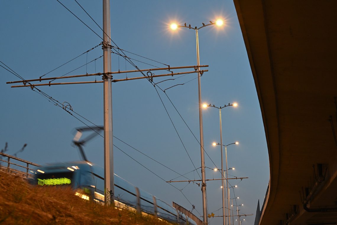 Noćna fotografija tramvaja u pokretu i ptica na stupovima rasvjete u Zagrebu