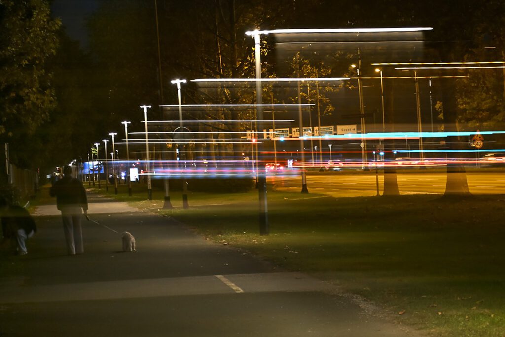 Noćna ICM fotografija s prolaznikom i prugastim svjetlosnim tragovima ulične rasvjete